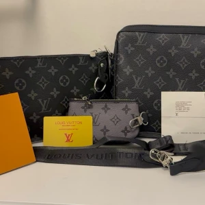  Monogram handväska - Snygg handväska i svart och grått monogrammönster. Väskan har en rektangulär form, avtagbar axelrem och matchande accessoarer som nyckelring och liten plånbok. För bättre bild skriv privat