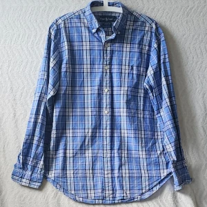 Blårutig skjorta från Ralph Lauren - Säljer en klassisk blårutig skjorta från Ralph Lauren i bomull. Skjortan har långärmad design, knappar framtill och en relaxed classic fit. Perfekt för dig som gillar en tidlös och snygg look med lite preppy vibes.