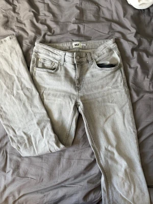 Ljusgrå raka jeans - Säljer ett par ljusgrå jeans med rak passform och klassisk femficksdesign. Jeansen har bälteshällor, knappgylf och är tillverkade i ett mjukt denimtyg. Perfekta för en avslappnad och stilren look.