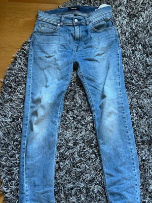 Ljusblå skinny jeans från Replay - Säljer ett par ljusblå skinny jeans från Replay med klassisk femficksmodell och snygga slitningar framtill. Jeansen har en läderpatch med Replay-logga bak i midjan och är tillverkade i mjuk denim med stretch för extra komfort. Med storlek 158 och 14a