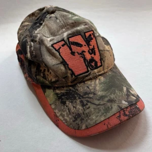 Camo Keps - Keps med camoflage och orangea detaljer. Jakt keps. Kepsen är smutsig, var medveten innan du köper. Skicka ett meddelande om du har frågor eller vill se fler bilder