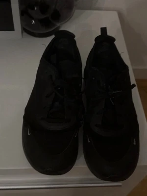 Svarta Nike Air Max sneakers - Snygga svarta Nike Air Max sneakers med klassisk siluett och diskreta vita detaljer. Skorna har snörning och synlig Air Max-dämpning i sulan för extra komfort. Perfekta för dig som gillar en stilren och sportig look.