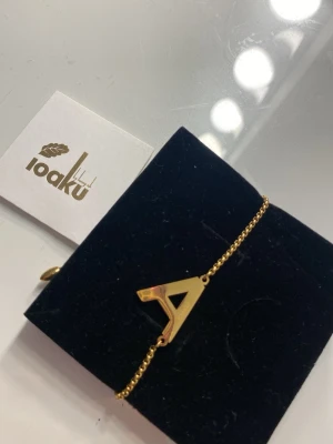 Guldarmband med bokstav A från Ioaku - Snyggt guldarmband från Ioaku med en stor bokstav A som hänge. Armbandet har en tunn kedja och justerbar låsning med två droppformade avslut. Perfekt för dig som vill ha en personlig touch på din stil. Så fint armband men väljer att sälja det eftersom jag inte använder guld. 