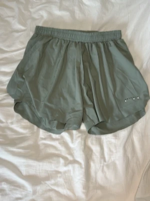 Gröna loose träningsshorts - Snygga gröna träningsshorts med loose fit och elastisk midja. Shortsen har en enkel design och är tillverkade i ett lätt syntetmaterial som passar perfekt för aktiva dagar. Liten logga med vita detaljer på ena benet. Rätt så stor i storleken