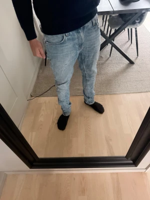 Ljusblå slim fit jeans herr - Säljer ett par ljusblå nudie jeans med klassisk femficksdesign och normal midja. Jeansen har en tvättad look och raka ben, perfekta för en avslappnad stil.