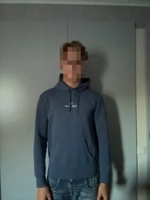 Blå hoodie Ralph lauren - En stilren blå hoodie med huva och dragsko samt broderad vit text på bröstet från polo Ralph lauren. Hoodien har en klassisk känguruficka framtill och ribbade muddar vid ärmslut och nederkant. Perfekt för en avslappnad look. Storlek S