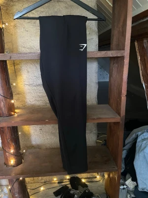 Svarta byxor från Gymshark - Snygga svarta byxor  från Gymshark med diskret logga på höften. De har en tight passform och är perfekta för träning eller chill. Tillverkade i stretchigt material som sitter skönt och följer kroppens rörelser.