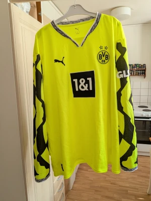 Gul Borussia Dortmund målvaktströja från Puma - Säljer en långärmad målvaktströja från Borussia Dortmund i neon-gult med svarta detaljer längs ärmarna. Tröjan har klubbmärke, Puma-logga och sponsortryck på bröstet. Perfekt för dig som vill sticka ut på planen. Storlek XXXL 