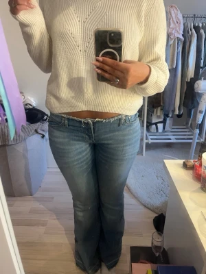 Blå bootcut jeans med rå kant - Säljer ett par ljusblå bootcut jeans med fransig, rå kant i midjan. Jeansen har klassisk femficksmodell och lätt slitna detaljer framtill. Perfekta för en avslappnad och trendig look.