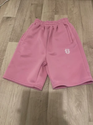 Rosa loose shorts med tryck - Säljer ett par rosa shorts med elastisk midja och lös passform. Shortsen har sidofickor, en bakficka och ett vitt tryck på ena benet. Perfekta för en avslappnad stil.