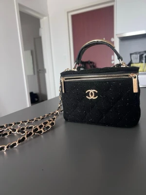 Svart  handväska  - Helt ny svart quiltad handväska  med guldfärgade detaljer och kedjerem. Väskan har dragkedja upptill, spegel i locket och flera kortfack inuti. Perfekt storlek för det viktigaste och riktigt snygg design!