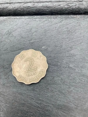 Två mynt: 2 dollar 1993 & 1 krona - Säljer två samlarmynt: ett 2 dollars mynt från 1993 med vågig kant och asiatiska tecken, samt ett svenskt 1 krona mynt med tre kronor och texten 'För Sverige i tiden'. Perfekt för dig som gillar att samla på unika mynt.