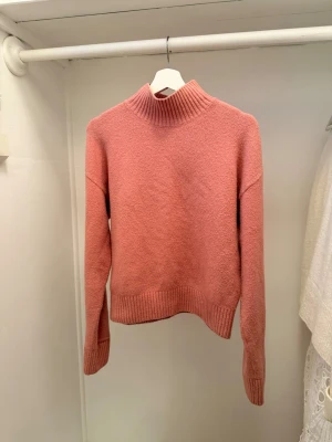 Rosa stickad polotröja - Mysig stickad tröja i dammig rosa färg med hög polokrage och ribbade muddar vid ärmslut och nederkant. Tröjan har en rak passform och är perfekt för kyliga dagar. Materialet ser mjukt och värmande ut.