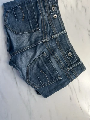 G-star shorts  - Snygga blå denimshorts med rå kant och slitna detaljer. Shortsen har fem fickor, bälteshällor och silverfärgade knappar. 