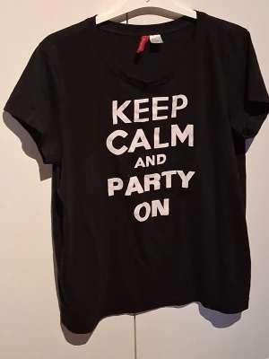 T-shirt med text - En svart t-shirt med texten "keep calm and party on" på framsidan.