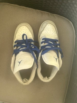 Vita sneakers med blåa skosnören - Snygga vita sneakers med blåa skosnören och perforerad tåbox. Skorna har en klassisk siluett och meshdetaljer runt ankeln. Perfekta för dig som gillar sportig stil och vill ha något som sticker ut med färgade snören. Priset är inte spikat i sten kom gärna med prisförslag