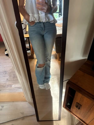 Ljusblå raka jeans med hål - Säljer ett par ljusblå jeans med rak passform och ett snyggt hål på ena knät. Jeansen har hög midja och är från Gina tricot. Passar någon som är runt 167