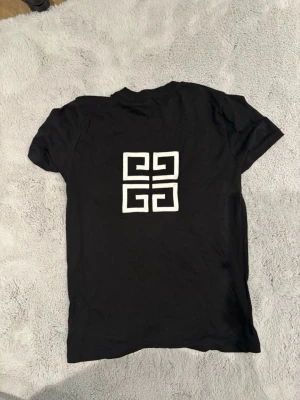 Svart t-shirt  - Säljer en svart t-shirt med en stor vit grafisk symbol på ryggen. T-shirten har korta ärmar och en klassisk passform. Perfekt för dig som gillar stilrena och moderna plagg.