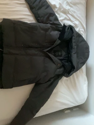 Svart pufferjacka från Canada Goose - Säljer en svart pufferjacka från Canada Goose i modellen Fusion, storlek XS passar S . Jackan har huva, dragkedja och tryckknappar framtill. Tillverkad i slitstarkt material och fodrad för extra värme. Perfekt för kalla vinterdagar. 