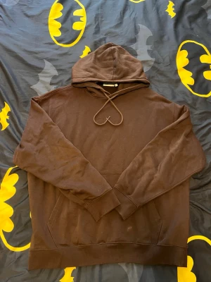 Brun hoodie från Weekday - Mysig brun hoodie från Weekday med klassisk huva och känguruficka framtill. Tillverkad i mjukt bomullsmaterial och har ribbade muddar vid ärmslut och nederkant. Perfekt för en avslappnad och stilren look. Oversize så S passar både M och L