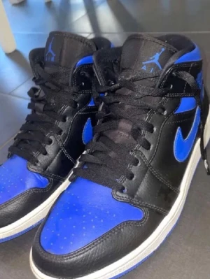 Jordan Air 1 Mid Royale blue - Säljer ett par Air Jordan 1 Mid sneakers i svart och blått läder. Skorna är i nyskick och alla tillbehör medföljer. 