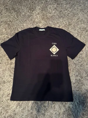 Svart Casa Blanca t-shirt med tryck - Snygg svart t-shirt från Casa Blanca med unikt grafiskt tryck både fram och bak. T-shirten har rund hals, korta ärmar och är gjord i mjukt bomullstyg. Perfekt för dig som gillar streetwear och vill sticka ut med cool design. Passar även M-L