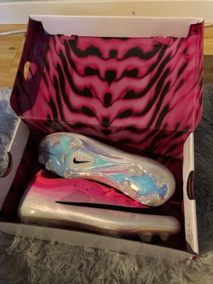 Nike rosa och vita fotbollsskor - Säljer ett par grymma fotbollsskor från Nike i en snygg rosa och vit färgkombination med svart swoosh. Skorna har en glansig, holografisk sula och är designade för bästa grepp på planen. Perfekta för dig som vill sticka ut och prestera på topp.
