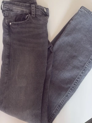 Grå low waist bootcut  jeans från Gina Tricot - Snygga grå jeans från Gina Tricot. Klassisk femficksdesign med knapp och dragkedja framtill. En knapp har gått av därbak annars som nya. 