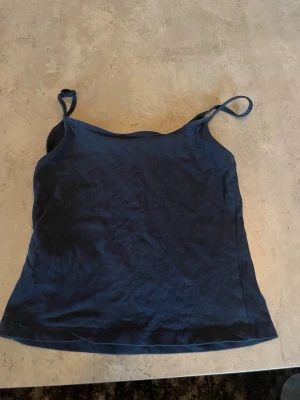 Mörkblå linnetopp från Gina Tricot - En enkel och stilren mörkblå linnetopp från Gina Tricot med smala axelband. Perfekt att matcha med jeans eller kjol för en avslappnad look. Tillverkad i mjuk bomull som känns skön mot huden.