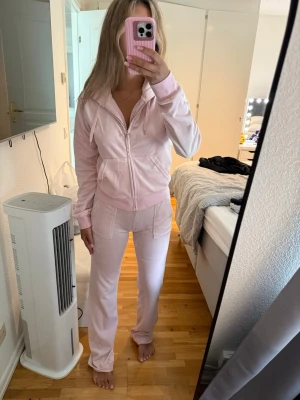 Ljusrosa mjukis set med fickor - Säljer ett mjukis set. mjukisbyxor i mjuk velour med raka ben och resår i midjan. Byxorna har fickor på sidorna och en relaxed passform som är perfekt för chill dagar hemma. Hoodie storlek M byxorna i xs. Finns några defekter som ni ser på bilden t.ex byxorna vid midjan lite missfärgat men inget som syns när tröjan är på. 