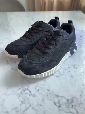Svarta sneakers med vit sula - Snygga svarta sneakers med ovandel i mocka och mesh, samt grovvit sula med coola detaljer på sidan. Skorna har svarta skosnören och en modern, sportig look som passar till många stilar.