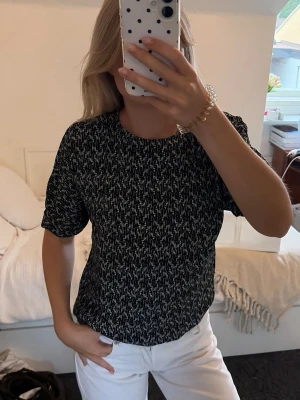 Svartvit mönstrad t-shirt - Säljer en svartvit t-shirt med korta ärmar och rund hals. Toppen har ett tätt, abstrakt mönster i vitt mot svart botten och är gjord i ett mjukt, stretchigt material. Perfekt till jeans eller kjol för en avslappnad look.