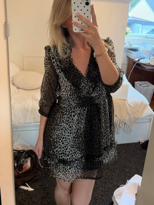 Leopardmönstrad kort klänning TSEGA - Säljer en kort klänning från TSEGA med leopardmönster i svart och beige. Klänningen har v-ringning, volangdetaljer och trekvartsärm. Tillverkad i ett lätt och luftigt material som ger en snygg siluett. Klänningen är i bra skick förutom att tyget lossnat på baksidan på höger arm, se bild. 