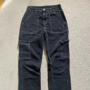 Mörka jeans i cargo-stil med många fickor och vita sömmar. Medium/hög midja. 