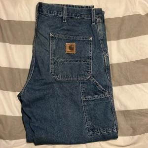 Carharrt arbetsbyxor  - Carpenter byxor från 90 talet. Väldigt stora i midjan så du behöver förmodligen bälte. Väldigt bra skick. Fin mörkblå färg.