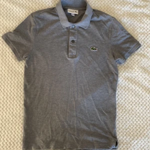 Grå Lacoste pikétröja  - Grå Lacoste pikétröja i vädkigt bra skick, har använt den ett fåtal gånger. Den här slimfit, alltså sitter rätt tajt och är i modellen xs.