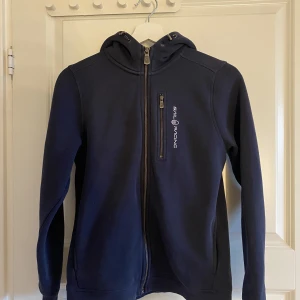 Mörk Blå SailRacing ZipUp Hoodie - Säljer min mörk blåa ”SailRacing” hoodie då den inte kommit till användning. Den är helt fläckfri. Säljer för 600 men priset kan diskuteras. Är flera intresserade blir de budgivning! Kontakta mig vid frågor, bilder och mer info!  Nypris 1000 