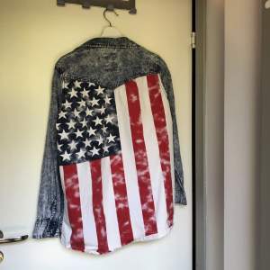 En oversized skjorta med den amerikanska flaggan på ryggen. Skjortan är gjord i bomull men ska likna jeanstyg. Inköpt på Bikbok för massa år sedan, knappt använd. Nyskick. 
