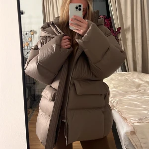 Äkta dunjacka, hm premium - En helt ny vinterjacka ifrån Hm's premium collektion förra året. Många snygga detaljer.Dunjacka i mycket fin brun/grå färg. Aldrig använd. Nypris 1699kr. Säljs tyvärr då den var för stor för mig💕världens finaste jacka