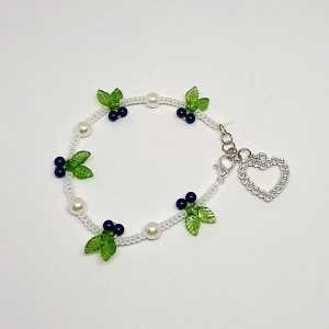 Blåbärs armband - Mörkblåa akrylpärlor med gröna blad och vita akrylpärlor. Glittrigt hjärta som charm. 