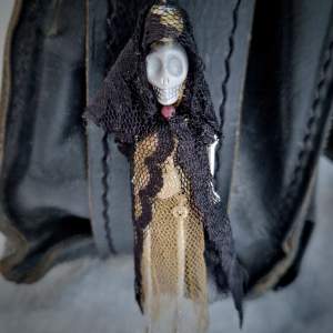 Väsksmycke eller på jackan: silverfärgad ledad figur med döskalle med handsydda spetskläder. Och en fastsydd äkta 