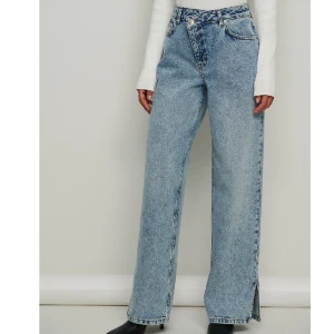 Jeans med asymmetrisk midja NA-KD - Syratvättade jeans med asymmetrisk midja från NA-KD💗Väldigt coola jeans som har en klassisk ljusblå färg, asymmetrisk midja och slits! De är använda en gång och är i utmärkt skick. 