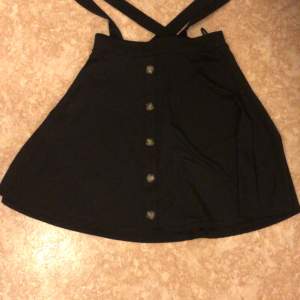 Medel lång svart kjol med hängslen och  fem knappar