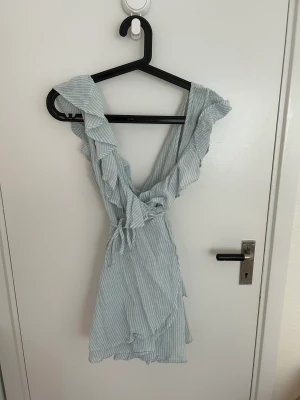 Omlottklänningen  - Blå och vitrandig kort omlottklänning med volang. 