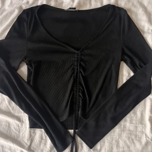 Svart v-ringad topp med knytning  - Svart långärmad topp med knytning som justerar längden på tröjan. Bra skick! 