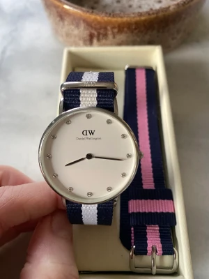 Daniel Wellington klocka i nyskick - Som ny! Endast använd 2 ggr. Nytt batteri isatt i Mars. Urtavlan är vitare än den ser ut på bilden.  Kommer med extra rem.   Nypris 1399kr  Kan levereras inom Alingsås och närhet (längs med E20 ner mot Lerum). Annars skicka, mottagare står för frakt. 