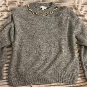 Grå tröja med guldkedja - Super mysig tjock tröja som är perfekt för kommande vinter.  Helt oanvänd pga för stor storlek. Den är i storlek S men passar mer som M/L (oversized).
