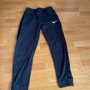 Svarta Nike byxor - Säljer nu mina svarta Nike byxor pga säljer nu mina Nike byxor pga att jag tappat intresset för dem/Dem här byxorna har ett Nike swosh märke längs sidan/det är ett litet hål under vänstra knät på byxorna/ men annars skick 6/10.