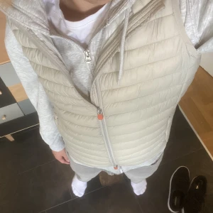 Väst - Beige Save the duck väst.  Skick 9/10. Storlek M. Kan kännas någorlunda tight beroende på hur tjock tröja du har. Orginalpris 1100 kr