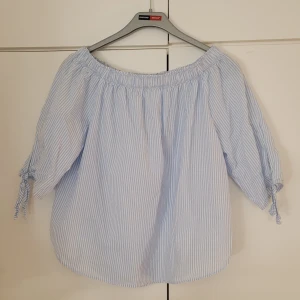 Offshoulder topp blå/vit - Offshoulder topp som är blå och vit randig, med knyten på armarna. Går även att använda som en vanlig topp utan offshoulder (som på bilden). Materialet är 100% bomull. 52 cm lång. Använd några få gånger. 